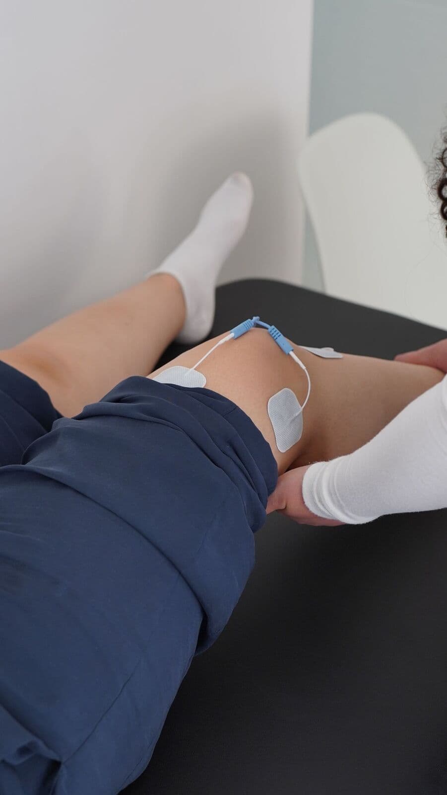 Électrodes d’électrostimulation posées sur un genou, jambe soutenue par la praticienne.